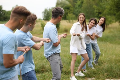 Photo of Team building. Group of happy people playing tug of war with rope outdoors