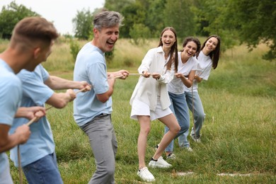 Photo of Team building. Group of happy people playing tug of war with rope outdoors