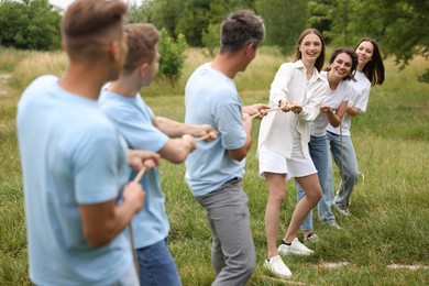 Photo of Team building. Group of happy people playing tug of war with rope outdoors