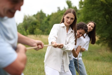 Photo of Team building. Group of happy people playing tug of war with rope outdoors