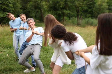 Photo of Team building. Group of happy people playing tug of war with rope outdoors
