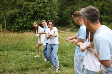 Photo of Team building. Group of happy people playing tug of war with rope outdoors
