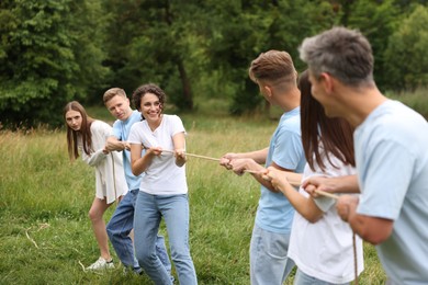 Photo of Team building. Group of happy people playing tug of war with rope outdoors