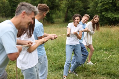 Photo of Team building. Group of happy people playing tug of war with rope outdoors