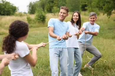 Photo of Team building. Group of happy people playing tug of war with rope outdoors