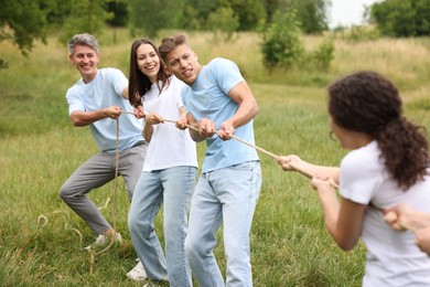 Photo of Team building. Group of happy people playing tug of war with rope outdoors
