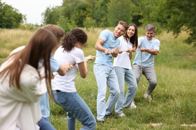 Photo of Team building. Group of happy people playing tug of war with rope outdoors