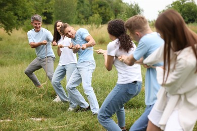 Photo of Team building. Group of happy people playing tug of war with rope outdoors