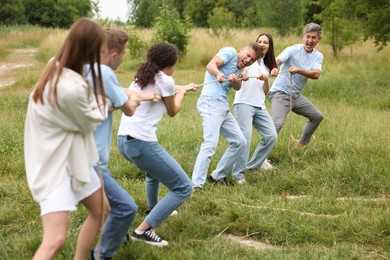 Photo of Team building. Group of happy people playing tug of war with rope outdoors