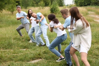 Photo of Team building. Group of happy people playing tug of war with rope outdoors