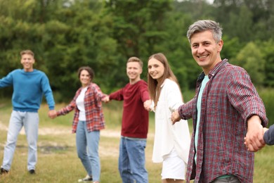 Photo of Team building. Group of happy people holding hands outdoors, selective focus
