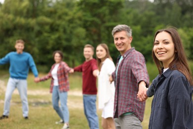 Photo of Team building. Group of happy people holding hands outdoors, selective focus