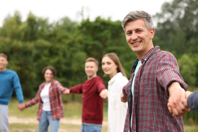 Photo of Team building. Group of happy people holding hands outdoors, selective focus