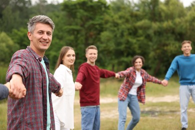 Photo of Team building. Group of happy people holding hands outdoors, selective focus