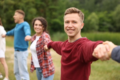 Photo of Team building. Group of happy people holding hands outdoors, selective focus