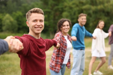 Photo of Team building. Group of happy people holding hands outdoors, selective focus