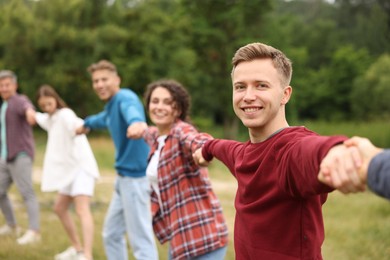 Photo of Team building. Group of happy people holding hands outdoors, selective focus