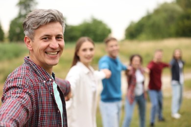 Photo of Team building. Group of happy people holding hands outdoors, selective focus