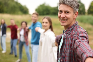 Photo of Team building. Group of happy people holding hands outdoors, selective focus