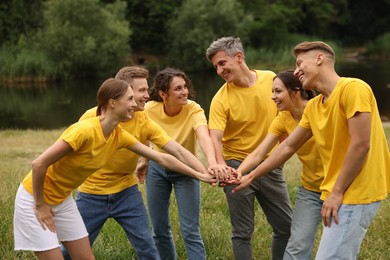 Photo of Team building. Group of happy people joining hands outdoors