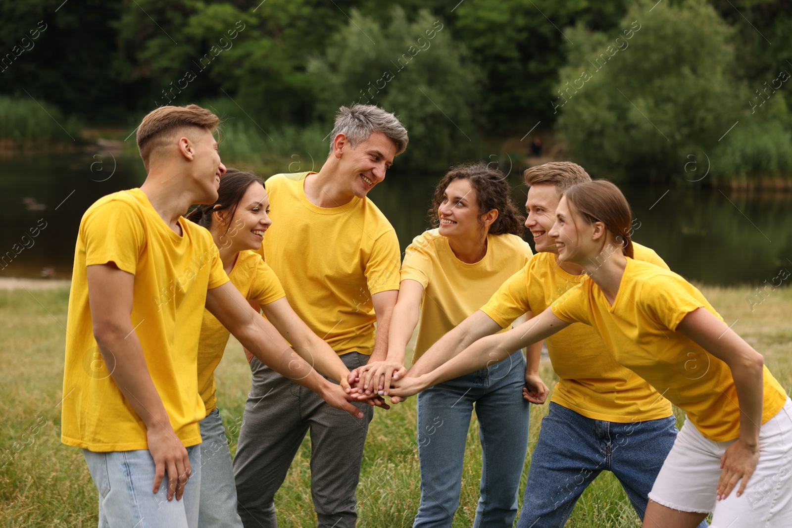 Photo of Team building. Group of happy people joining hands outdoors