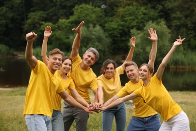Photo of Team building. Group of happy people joining hands outdoors