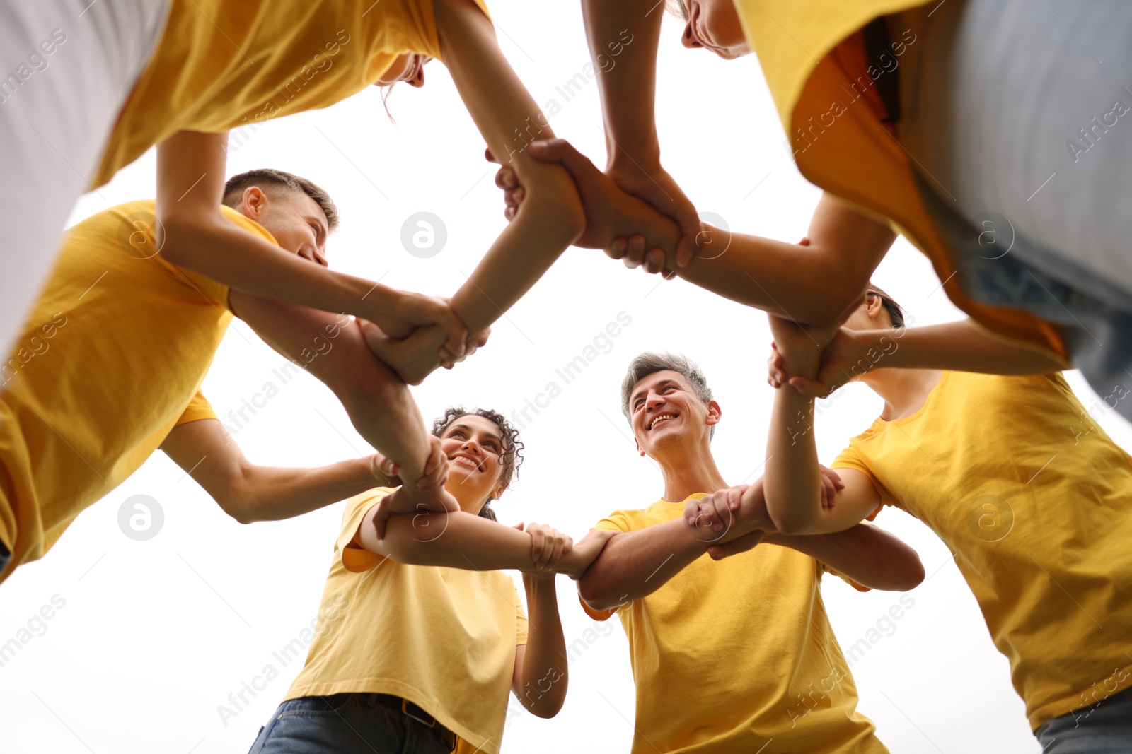 Photo of Team building. Group of happy people joining hands outdoors, bottom view