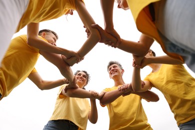 Photo of Team building. Group of happy people joining hands outdoors, bottom view