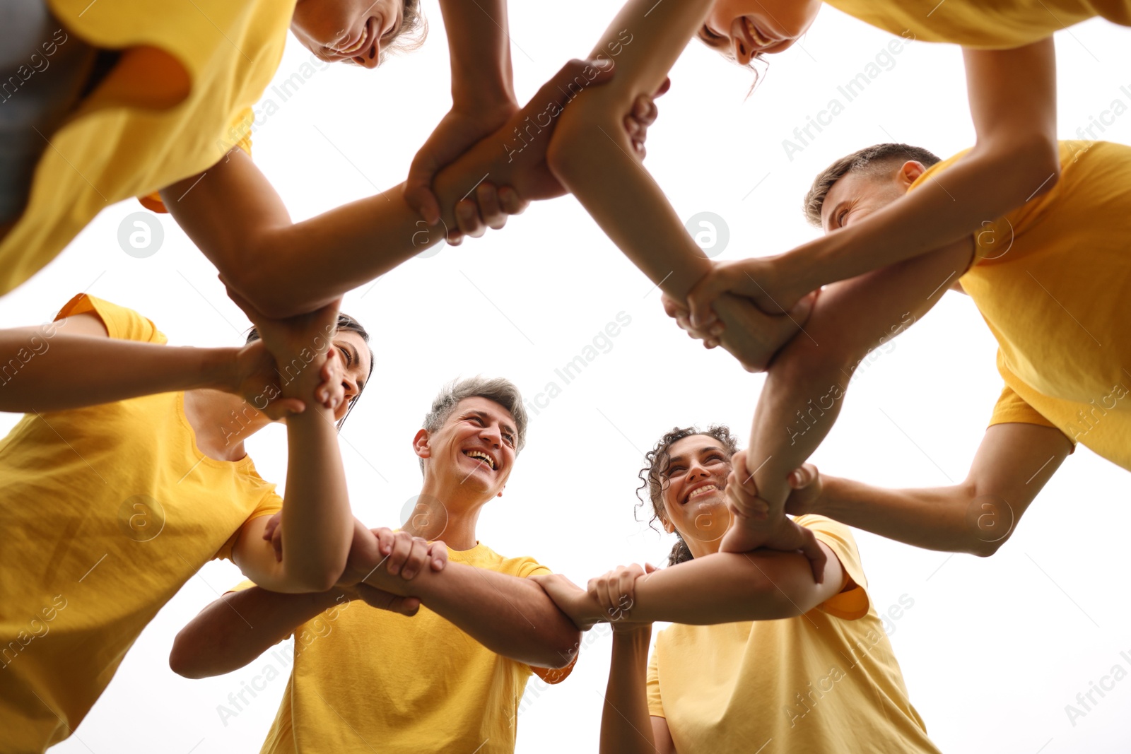 Photo of Team building. Group of happy people joining hands outdoors, bottom view