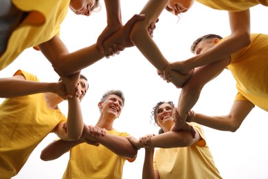 Photo of Team building. Group of happy people joining hands outdoors, bottom view