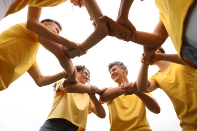 Photo of Team building. Group of happy people joining hands outdoors, bottom view