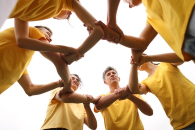 Photo of Team building. Group of happy people joining hands outdoors, bottom view