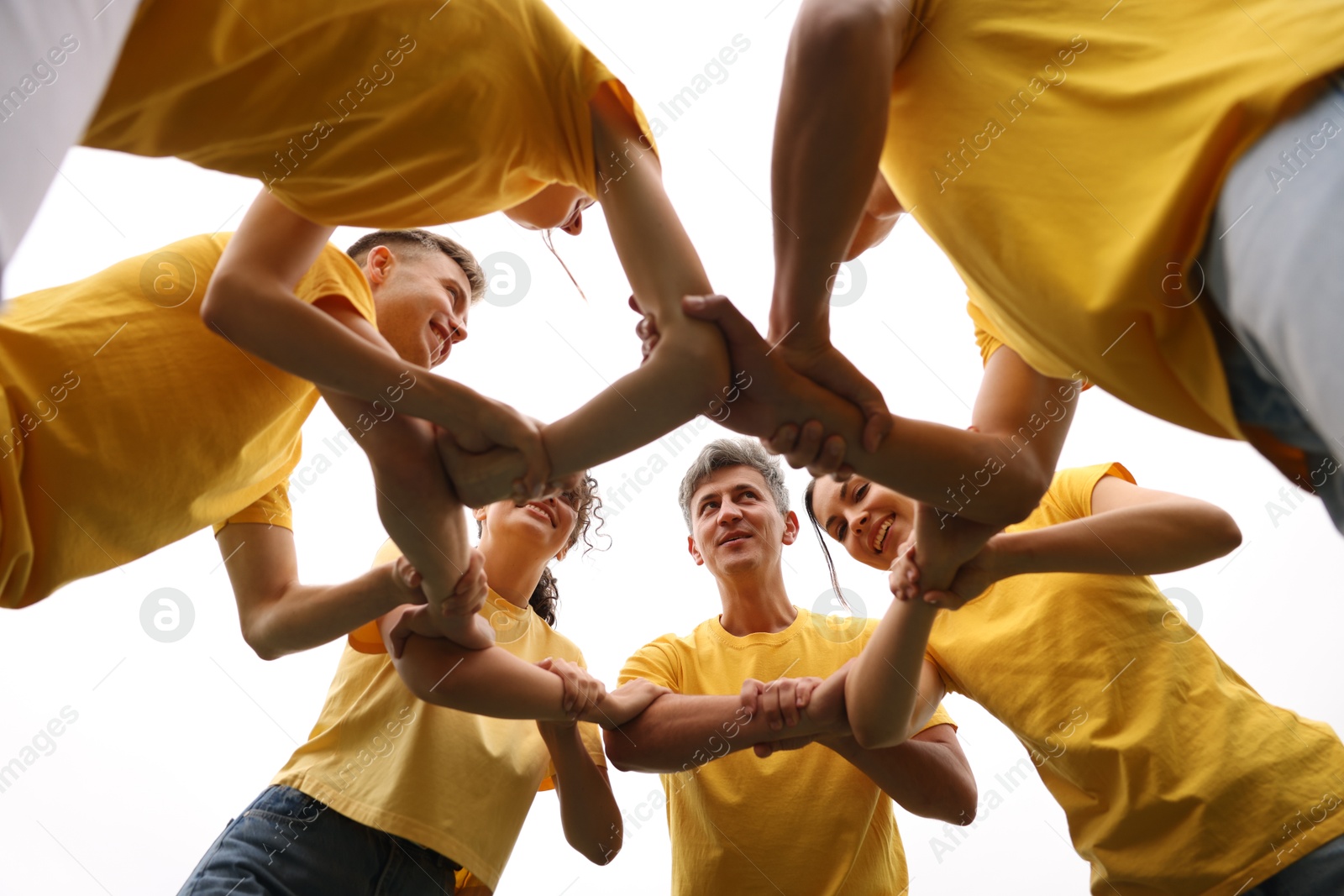 Photo of Team building. Group of happy people joining hands outdoors, bottom view