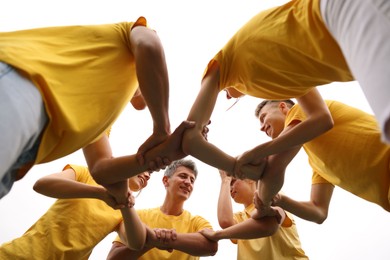Photo of Team building. Group of happy people joining hands outdoors, bottom view