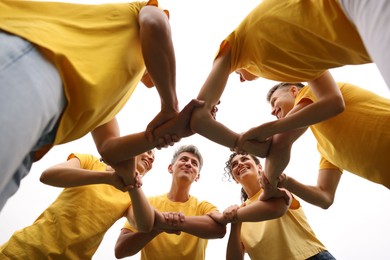 Photo of Team building. Group of happy people joining hands outdoors, bottom view