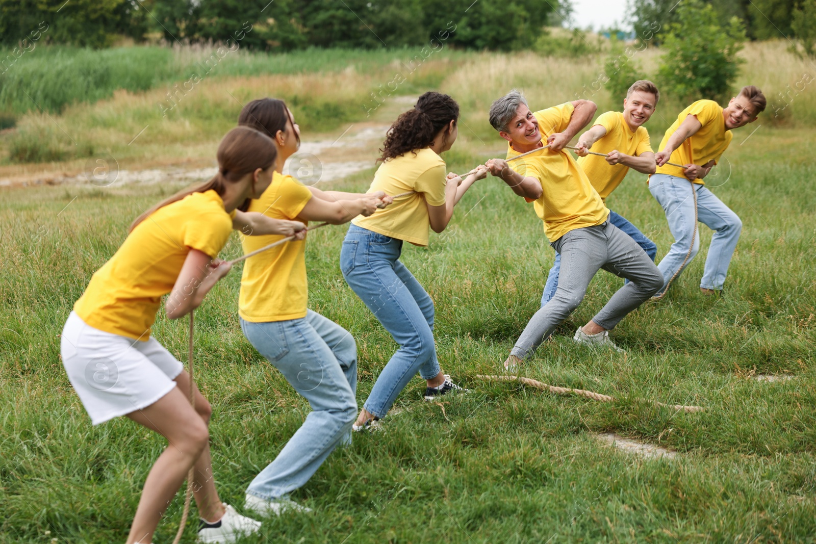 Photo of Team building. Group of happy people playing tug of war with rope outdoors