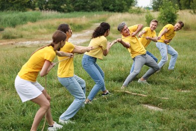 Photo of Team building. Group of happy people playing tug of war with rope outdoors