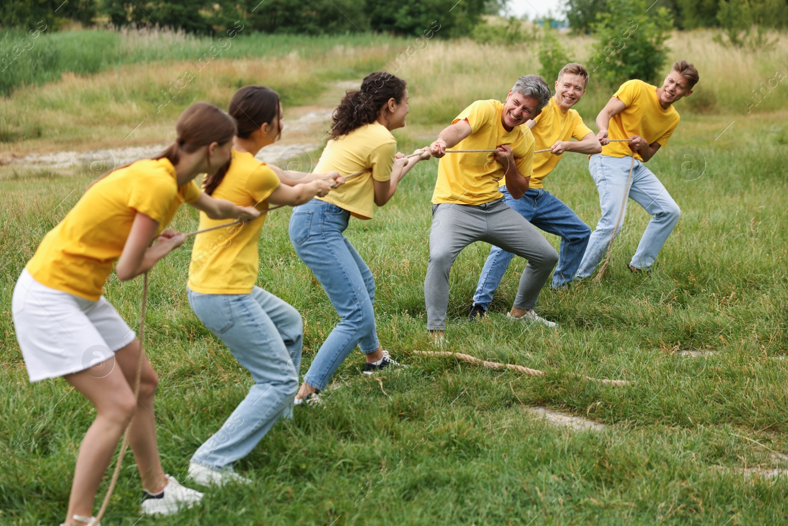 Photo of Team building. Group of happy people playing tug of war with rope outdoors