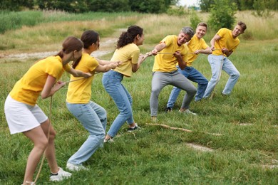 Photo of Team building. Group of happy people playing tug of war with rope outdoors