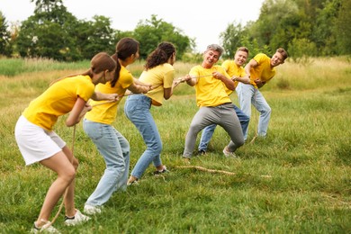 Photo of Team building. Group of happy people playing tug of war with rope outdoors