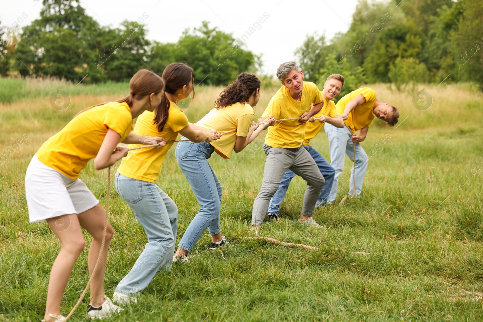 Photo of Team building. Group of happy people playing tug of war with rope outdoors