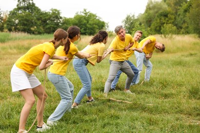 Photo of Team building. Group of happy people playing tug of war with rope outdoors