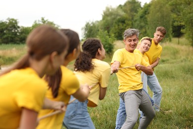 Photo of Team building. Group of happy people playing tug of war with rope outdoors