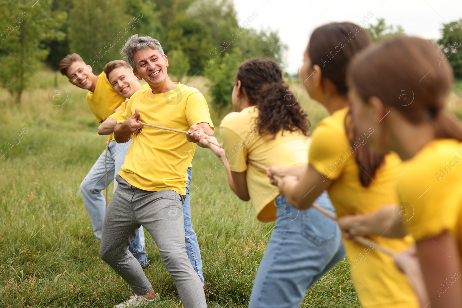 Photo of Team building. Group of happy people playing tug of war with rope outdoors