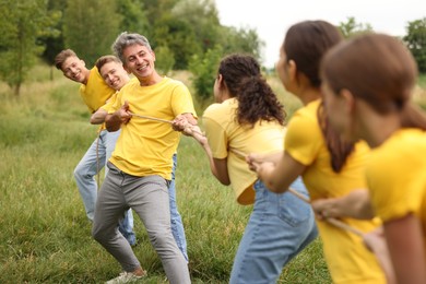 Photo of Team building. Group of happy people playing tug of war with rope outdoors
