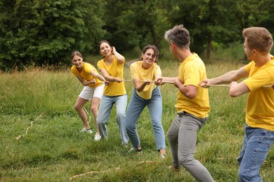 Photo of Team building. Group of happy people playing tug of war with rope outdoors
