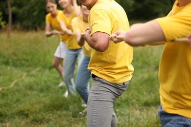 Photo of Team building. Group of people playing tug of war with rope outdoors, closeup