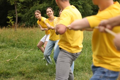 Photo of Team building. Group of happy people playing tug of war with rope outdoors