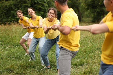 Photo of Team building. Group of happy people playing tug of war with rope outdoors