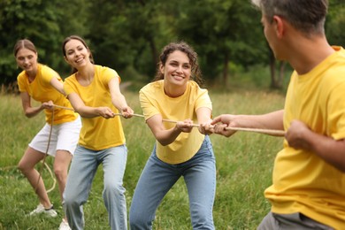 Photo of Team building. Group of happy people playing tug of war with rope outdoors